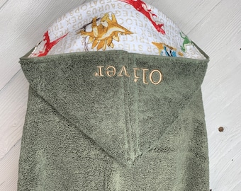 May include: A green hooded towel with the name "Oliver" embroidered on the front. The hood is lined with a white fabric featuring a dinosaur print.