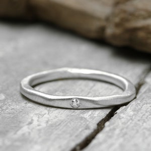 Könnte beinhalten: Ein schlichter Silberring mit einem kleinen, klaren Diamanten in der Mitte.