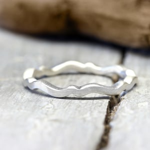 Könnte beinhalten: Ein silberner Ring mit einem wellenförmigen, strukturierten Design. Der Ring ist aus Metall und hat eine gebürstete Oberfläche.