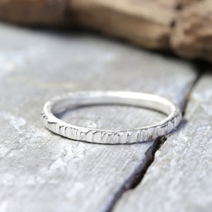 Könnte beinhalten: Ein silberner Ring mit einer strukturierten, gehämmerten Oberfläche. Der Ring ist schlicht und elegant und wäre ein tolles Schmuckstück für jeden Tag.