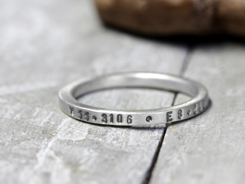 May include: A silver ring with the inscription "N 55.3106  E 8.201" engraved on the band.