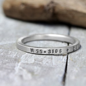 May include: A silver ring with the coordinates "N 55.3106" engraved on it.