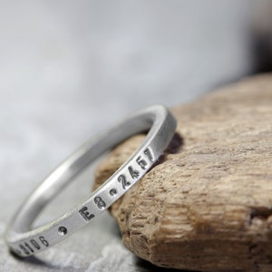 May include: A silver ring with a series of numbers engraved around the band. The ring is resting on a piece of weathered wood.