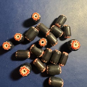 May include: A collection of black and white glass beads with red flower designs. The beads are cylindrical and have a glossy finish.