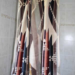 May include: A patterned bath towel with a geometric design in shades of beige, brown, navy, and red. The towel is hanging from a white shower rod. The design features triangles and diamond shapes.