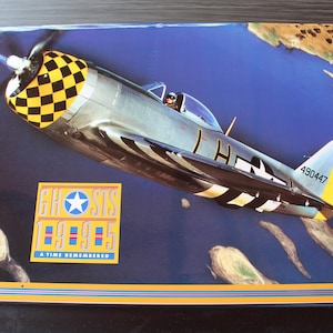 May include: A vintage poster featuring a silver airplane with a black and yellow checkered nose and a yellow tail. The plane is set against a blue sky with landmasses. The poster includes the text "GHOSTS 99-95 A TIME REMEMBERED."
