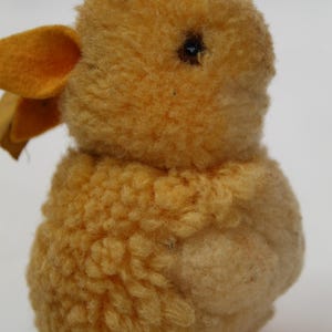 May include: A vintage, plush yellow duck toy with a textured, fuzzy body and small, dark eye. The duck has a small, orange beak and a soft, rounded shape, suggesting a classic children's toy.