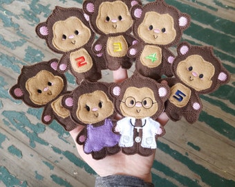 May include: Set of seven brown felt finger puppets shaped like monkeys. Each monkey has a different embroidered design, including numbers 1 through 5, a doctor's stethoscope, and a green leaf.