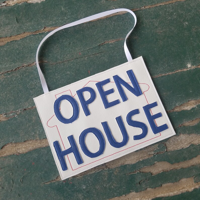 May include: White fabric sign with a blue stitched outline of a house and the words "OPEN HOUSE" in blue stitched letters.