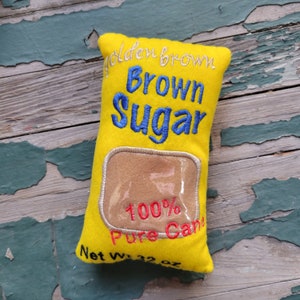 May include: A yellow felt pillow shaped like a brown sugar bag with the text "Golden Brown Brown Sugar 100% Pure Cane Net Wt. 32 oz" embroidered on it.