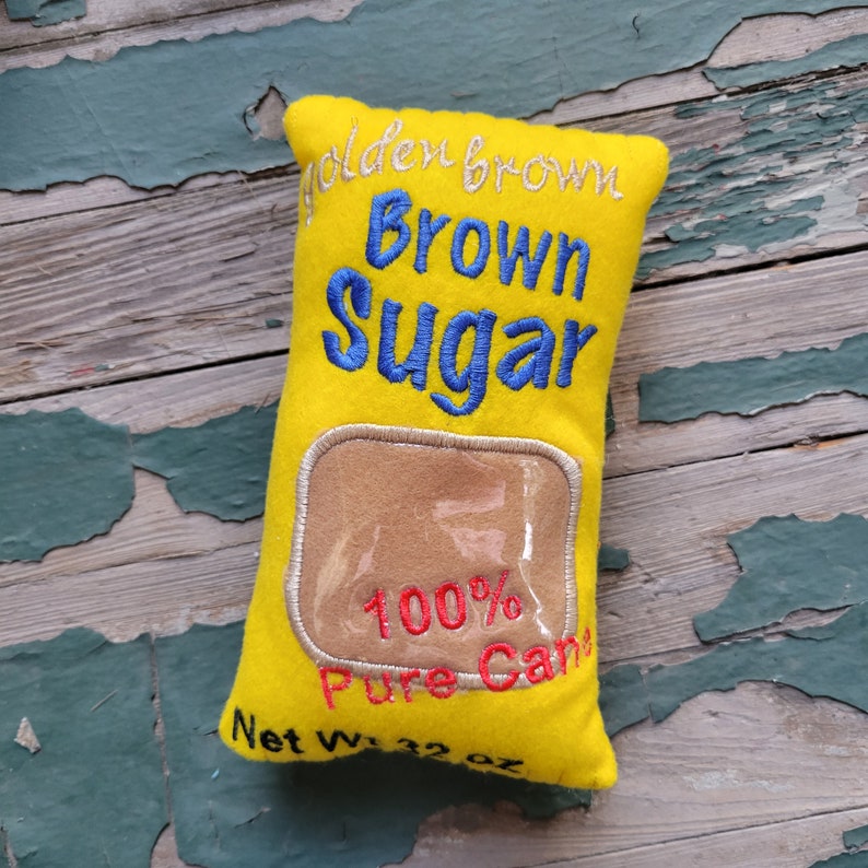 May include: A yellow felt pillow shaped like a brown sugar bag with the text "Golden Brown Brown Sugar 100% Pure Cane Net Wt. 32 oz" embroidered on it.