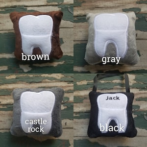 May include: Four plush tooth-shaped pillows in different colours: brown, grey, grey with "castle rock" text, and black with "Jack" text.
