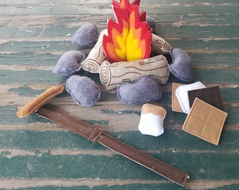 May include: Felt play set for pretend camping with a campfire, logs, marshmallows, and a stick. The campfire is red and yellow, the logs are brown, the marshmallows are white, and the stick is brown.