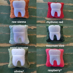 May include: Four plush tooth-shaped cushions in different colours: raw sienna, rhythmic red, pastel turquoise, and mountain view. The cushions are all the same size and shape, and they have a white tooth embroidered on the front.