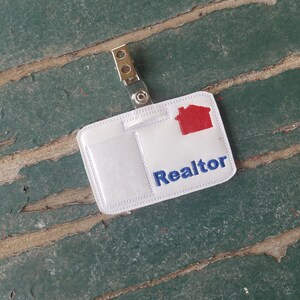May include: White plastic realtor ID badge with a red house icon and blue text that says "Realtor".