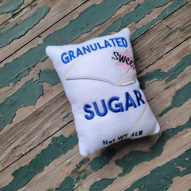 May include: White plush pillow shaped like a sugar bag with the text "GRANULATED Sweet SUGAR Net WT 4LB" embroidered on it.