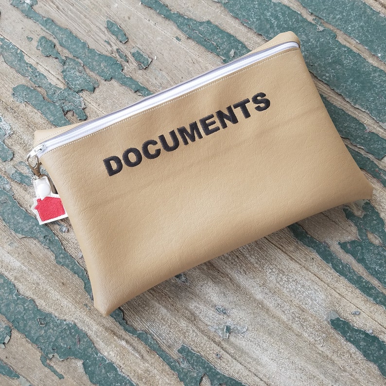 May include: A tan leather pouch with a white zipper and the word "DOCUMENTS" embroidered in black.