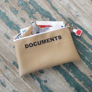 May include: A tan leather pouch with a zipper closure and the word "DOCUMENTS" printed in black. The pouch is open and contains various papers and a small key chain.