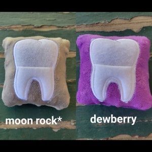 May include: Two plush tooth-shaped pillows, one in a light brown colour with the text "moon rock*" and the other in a purple colour with the text "dewberry".