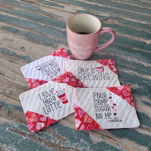 May include: Four quilted fabric coasters with red and white hearts and coffee-themed embroidery. The coasters feature the phrases "emotional support coffee cup", "Love is brewing", "Love you a latte", and "Pour some sugar on me - coffee".