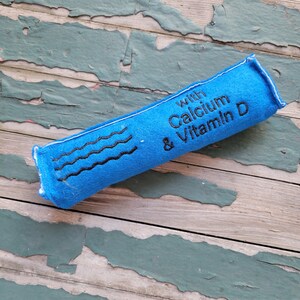 May include: Blue fabric tube with the text "with Calcium & Vitamin D" embroidered on it.