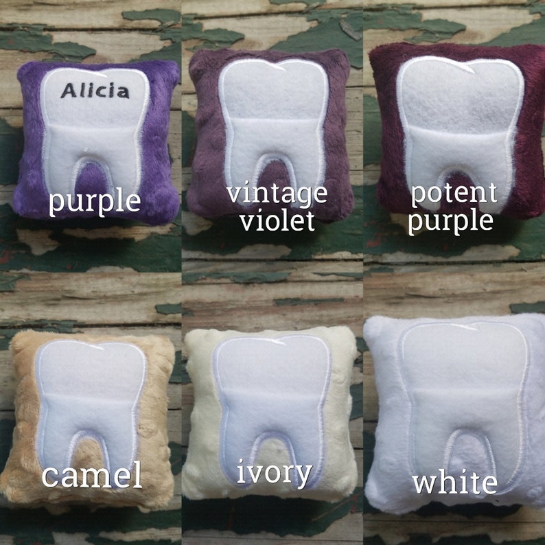 May include: Six plush tooth pillows in different colours: purple, vintage violet, potent purple, camel, ivory, and white. Each pillow has a white embroidered tooth on the front. The pillows are arranged in two rows of three.