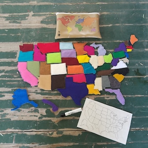 May include: A felt map of the United States with each state a separate piece. The map is laid out on a wooden surface with a blank outline map and a marker nearby. The map is a learning tool for children.