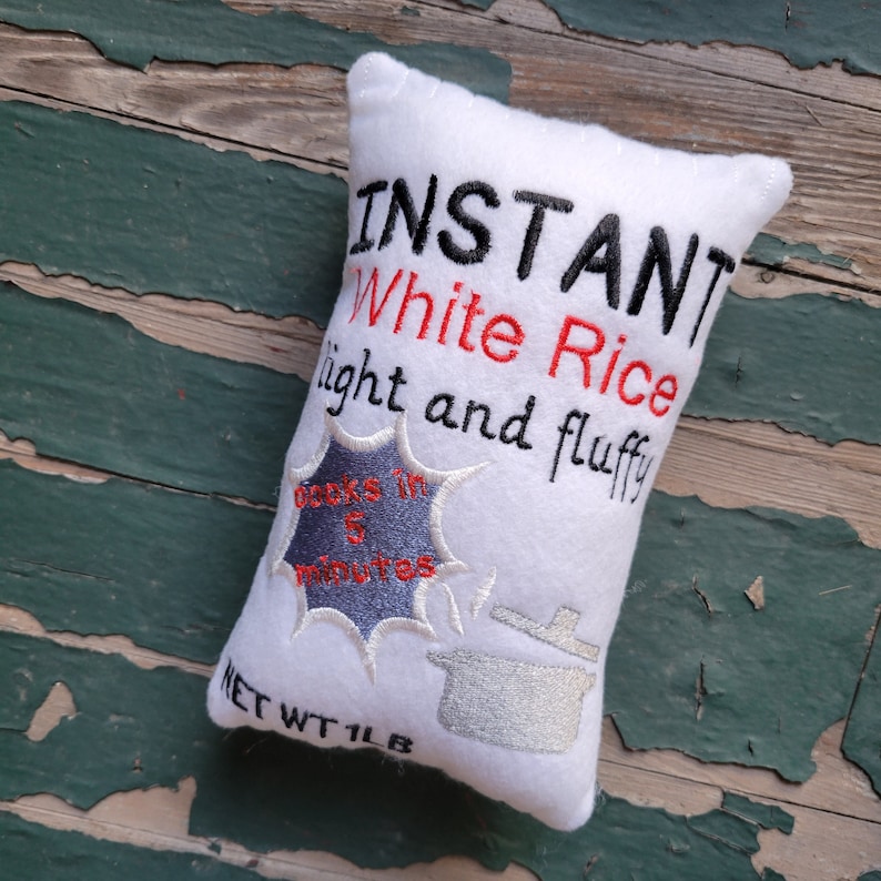 May include: White pillow shaped like a rice box with the text "INSTANT White Rice light and fluffy cooks in 5 minutes" and a silver pot icon. The text "NET WT 1 LB" is at the bottom.