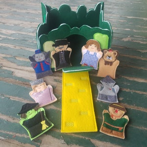 May include: A felt puppet theater set with a green felt castle and a yellow felt path. The set includes 8 felt finger puppets: Dorothy, the Scarecrow, the Tin Man, the Cowardly Lion, the Wicked Witch of the West, the Wizard of Oz, Glinda the Good Witch, and a flying monkey.