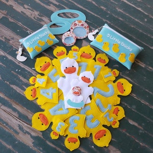 May include: A collection of felt duck-themed educational toys. Includes yellow duck-shaped numbers, duck finger puppets, and blue pouches with the text "5 Little Ducks". Decorative duck-shaped accessories are also present.