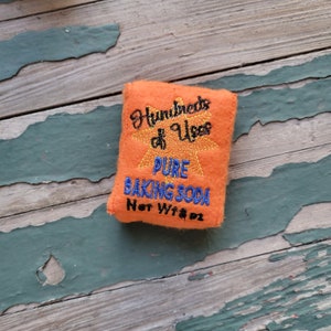 May include: Orange felt pouch with embroidered text that reads "Hundreds of Uses Pure Baking Soda Net Wt 8 oz".