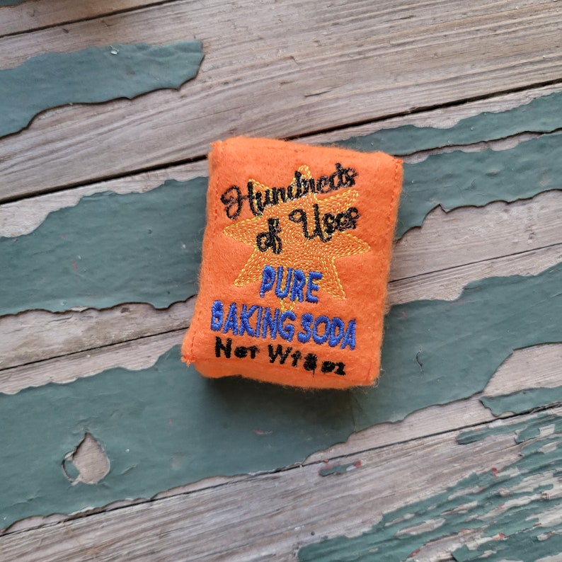 May include: Orange felt pouch with embroidered text that reads "Hundreds of Uses Pure Baking Soda Net Wt 8 oz".