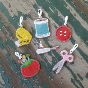 May include: Six colorful embroidered ornaments with sewing-themed designs. The ornaments include a spool of thread, a button, a thimble, a pair of scissors, a needle and thread, and a measuring tape.