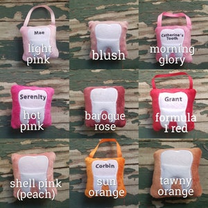 May include: Nine plush tooth-shaped cushions in a variety of colours, including light pink, blush, morning glory, hot pink, baroque rose, formula 1 red, shell pink (peach), sun orange, and tawny orange. Each cushion features a white embroidered tooth and a name or phrase on the front.