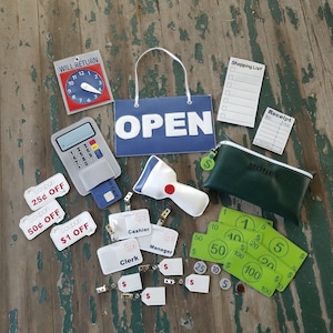May include: A play set for a pretend store or shop, featuring a cash register, a scanner, a credit card, coupons, play money, and a sign that says "OPEN".