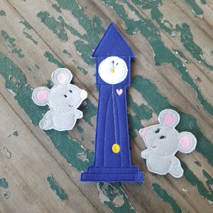 May include: Two gray felt mice with pink ears and black eyes stand next to a blue felt clock with a white face and a gold pendulum. The clock has a heart on the bottom.