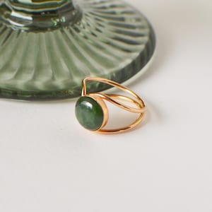 May include: A gold ring with a green jade stone set in the centre. The ring has a double band design.