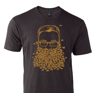May include: A dark heather grey t-shirt with a graphic of a person with a beard made of bees. The graphic is in a gold color.