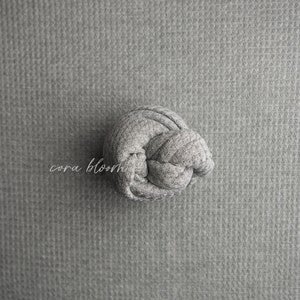 May include: A gray knitted fabric ball, tied in a knot, on a gray textured background.