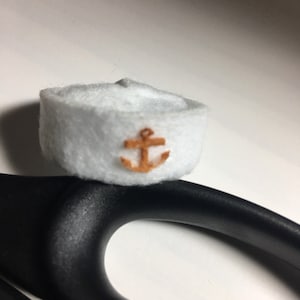 May include: A white felt sailor hat with a brown anchor embroidered on the front.
