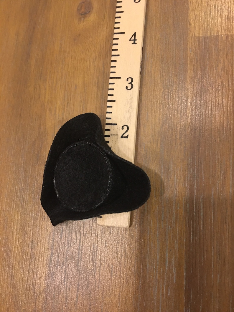 May include: A black felt pirate hat with a round crown and a brim that curves up on the sides. The hat is about 2 inches in diameter.