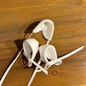 May include: Two white felt baby shoes with white satin ribbon ties. The shoes are tied in bows.