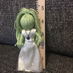 May include: A handmade doll with green yarn hair, a white dress, and a blue gemstone necklace. The doll is approximately 5 inches tall.