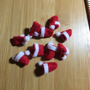 May include: A collection of nine miniature felt Santa hats in red and white. The hats are scattered on a wooden surface.