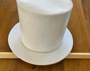 Puede incluir: Un sombrero de copa blanco de fieltro con un ala ancha. El sombrero está sobre una superficie de madera.