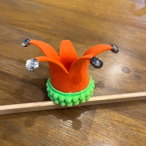 May include: A bright orange felt jester's hat with a green pom-pom trim and silver rhinestones.