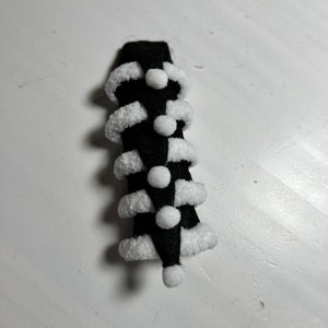 May include: Black and white Christmas tree ornament with white pom-poms and a white fur trim.