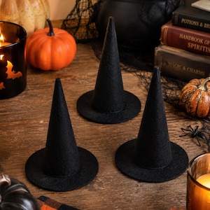 May include: Three black felt witch hats with pointed crowns and circular brims. The hats are solid black in color and feature a smooth, matte texture. Each hat is constructed with a tall, conical top section and a flat, round base.