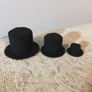May include: Three black felt top hats of varying sizes. The hats are arranged in a row from largest to smallest.