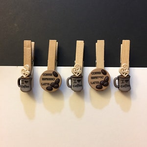 May include: Five wooden clothespins with coffee-themed decorations. Each clothespin has a round, brown and white design with a coffee cup and text that reads "I love coffee" or "Coffee Espresso Latte".